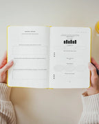 Person holding wellness journal with a pen and a glass of functional recovery soda on a light background